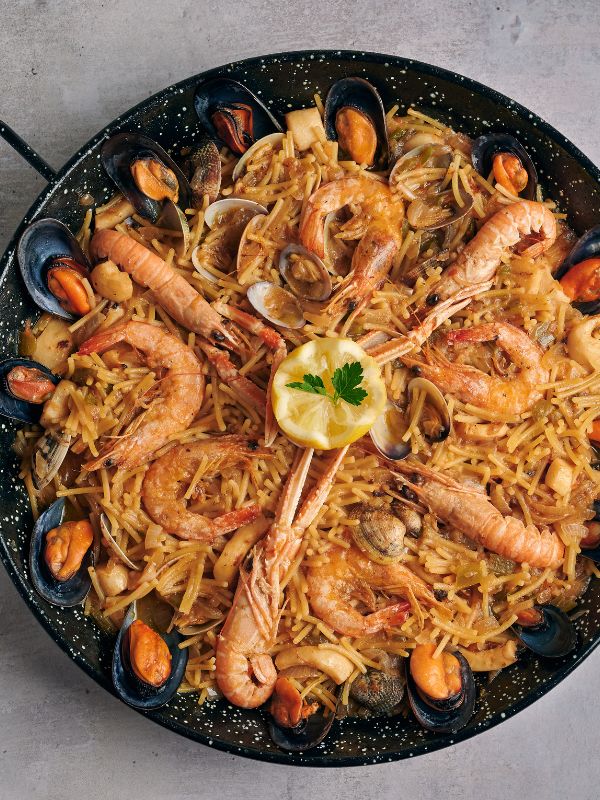 Paella with pasta and seafood in a pan.