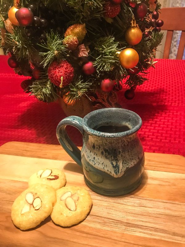 Spanish almond cookies on a wooden plate, next to a cup of hot drink and in the background there's Christmas decorations.