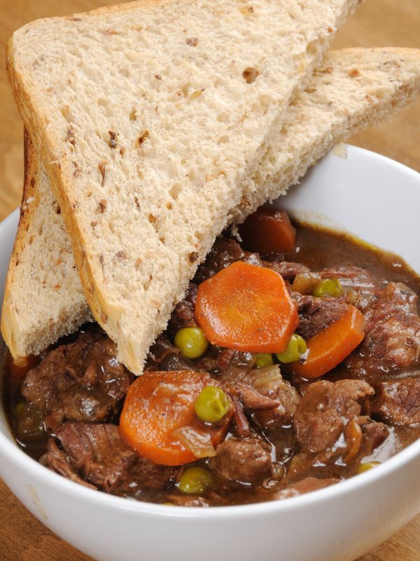 Spanish lamb stew served in a white bowl with 2 slices of bread