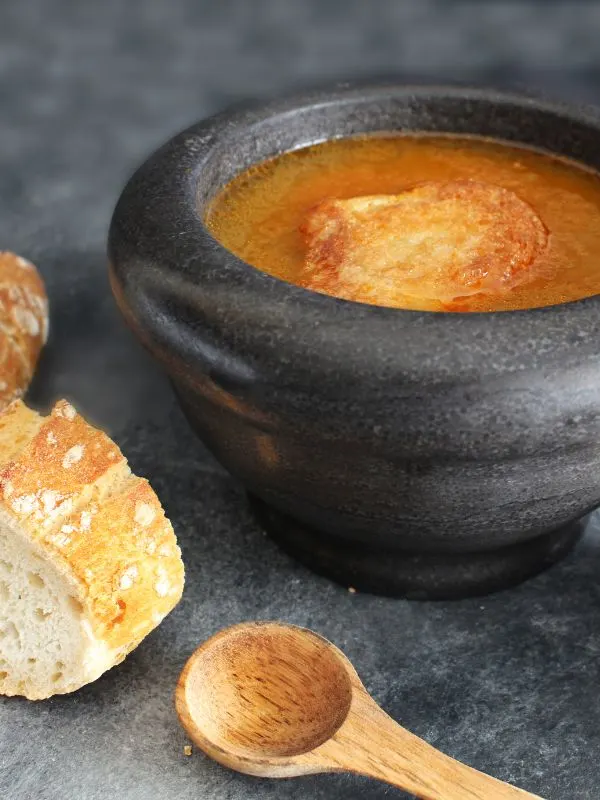 Spanish potato soup in a black bowl next to fresh bread