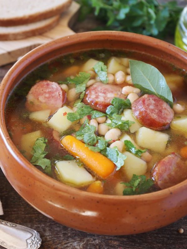 caldo gallego soup in a clay bowl next to 2 slices of bread on a wooden table. 25 Ideas for the Best Spanish Themed Party 