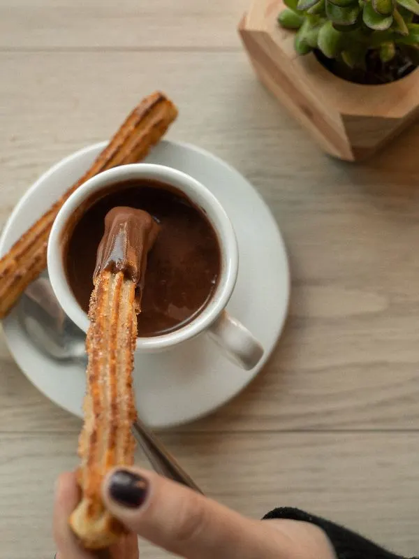 baked churros dipped in spanish chocolate, served on a wooden table.