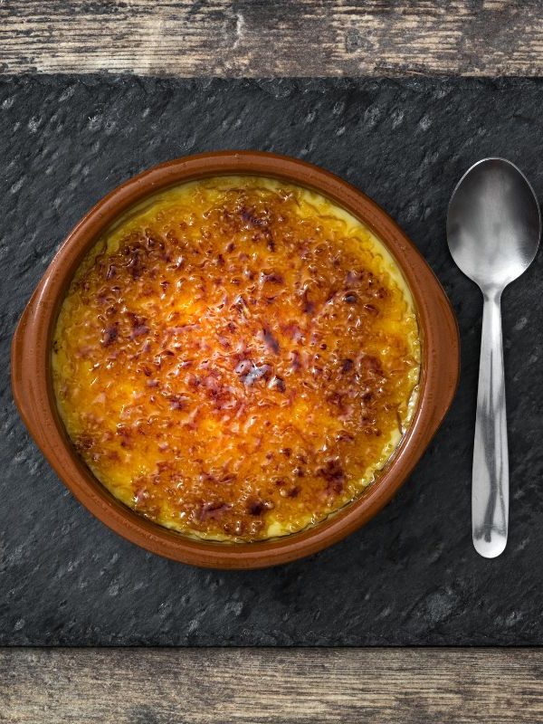 crema catalana dessert in a clay pot, on a wooden table and next to it there's a spoon. 25 Ideas for the Best Spanish Themed Party 