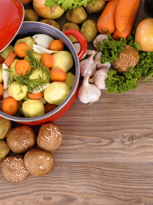 ingredients for the spanish veggie stew such as potatoes, carrots, mushrooms, onion and garlic on a wooden table.