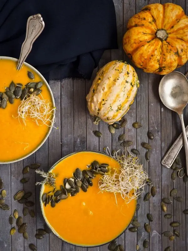 pumpkin soup in 2 bowl next to a small pumpkin