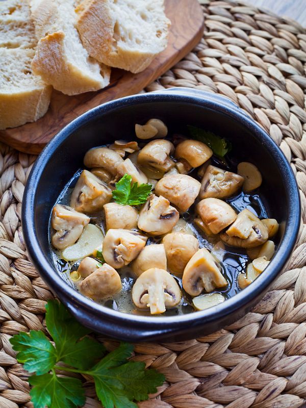 spanish garlic mushrooms in a pot with fresh parsley next to slices of bread.