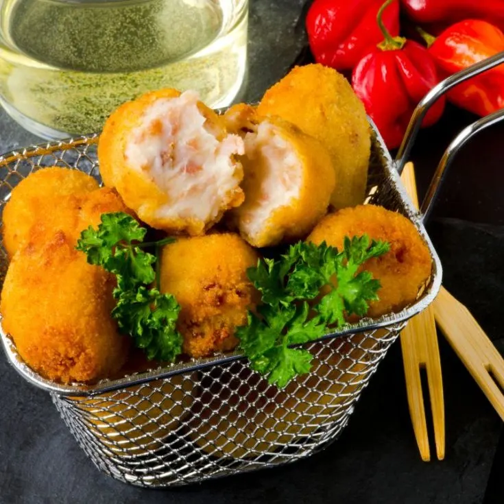 spanish ham croquettes in a serving basket on a black plate next to red peppers and a drink - Easy Spanish Ham Croquettes Recipe
