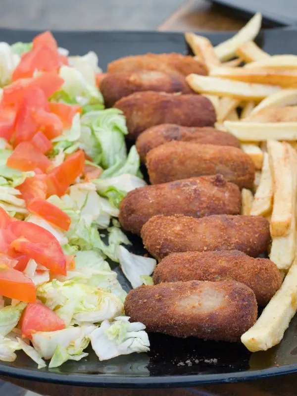 spanish chorizo croquettes with salad and fries on a black plate