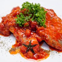 spanish pork chops with tomato sauce, on a white plate decorated with parsley,