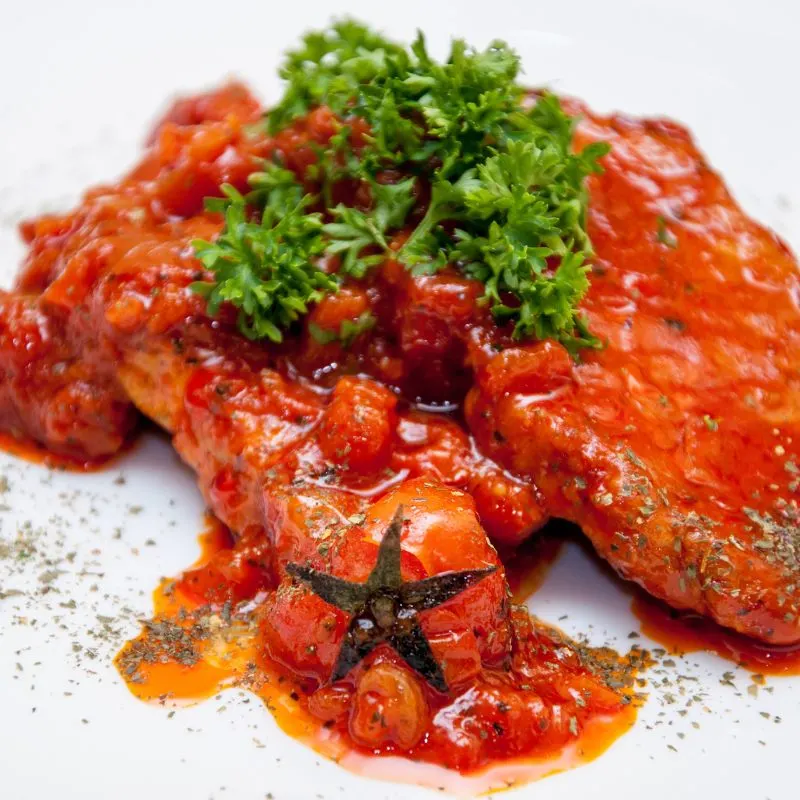 Spanish pork chops with tomato sauce, on a white plate decorated with parsley. Perfect Spanish Pork Chops Recipe