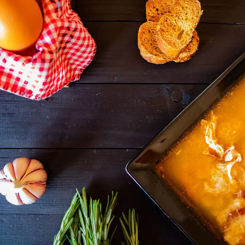 spanish potato soup in a bowl, on a wooden table, next to eggs, garlic, bread. Warming Spanish Potato Soup Recipe