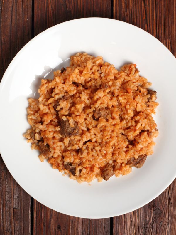 spanish rice with ground beef on a white plate, on a wooden table.