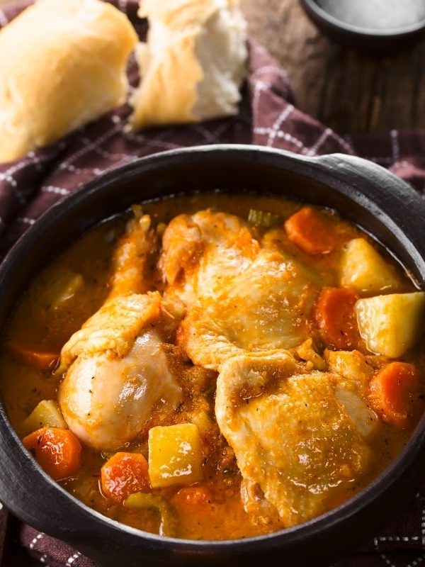 spanish chicken stew in a pot with bread on the side. 