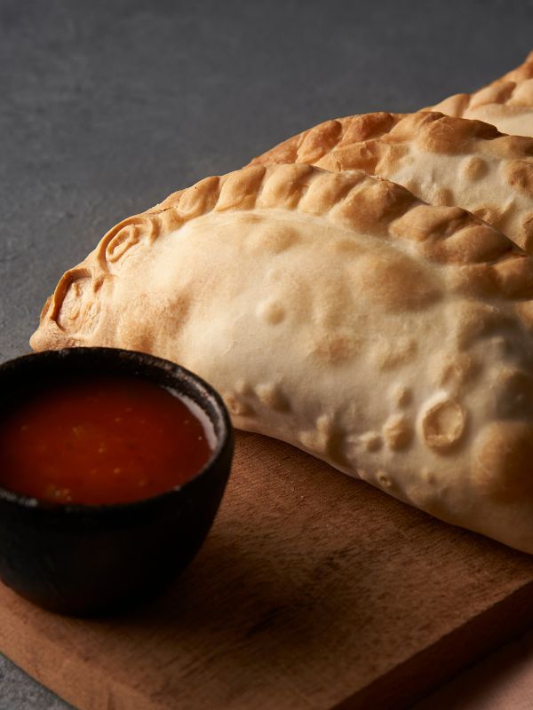 vegetarian empanadas on a wooden plate next to a red sauce.