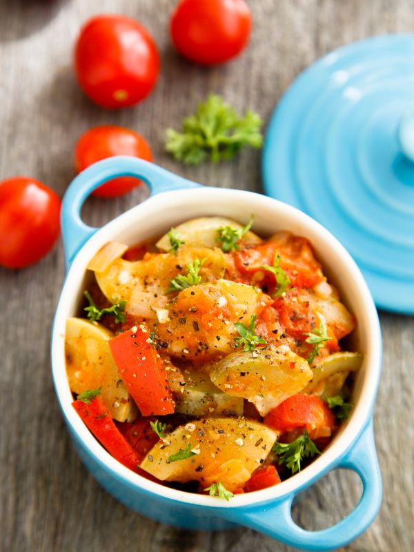 vegetarian spanish dish in a blue pot, on a wooden table with tomatoes next to it.