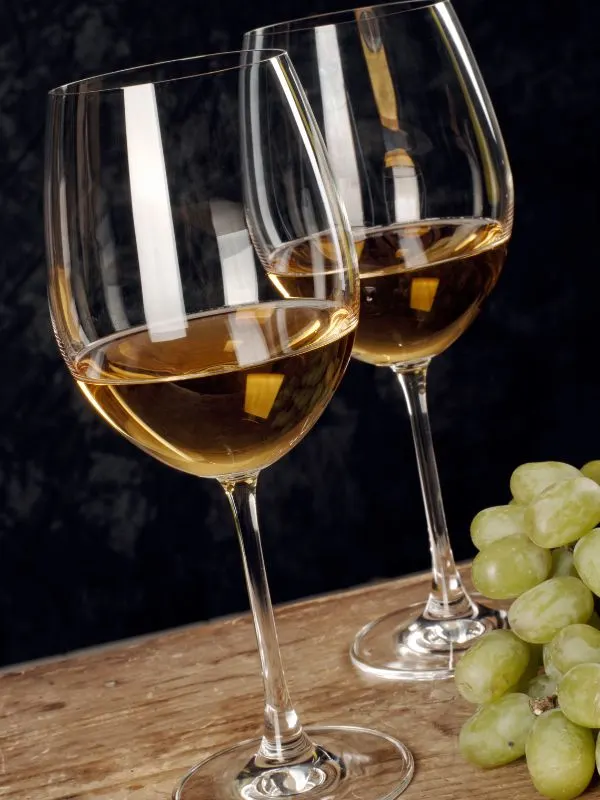 2 glasses of Godello white wine on a wooden table with grapes next to it. 