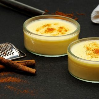 Natillas De Leche in 2 bowls next to some cinnamon on a black surface. Authentic Spanish Sweets