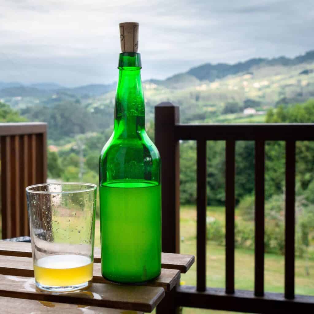 a bottle of cider and a glass sitting on a table with a nature on the background