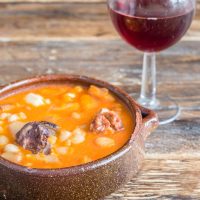 Spanish chickpea soup in a clay bowl next to a glass o wine