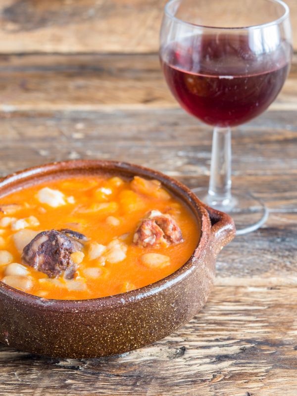 Spanish chickpea soup in a clay bowl next to a glass o wine