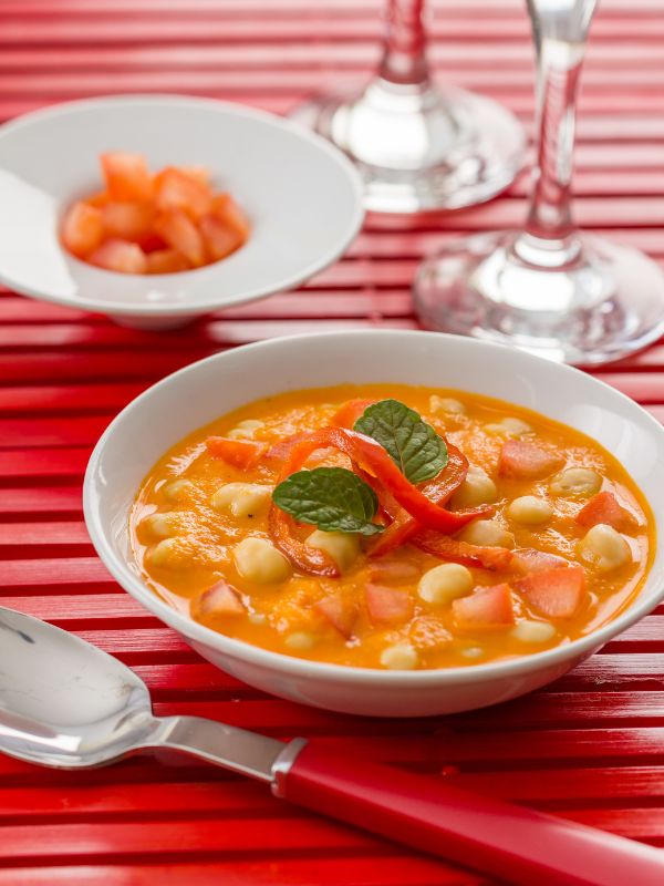 garbanzo bean soup with ham in a white bowl on a red surface.