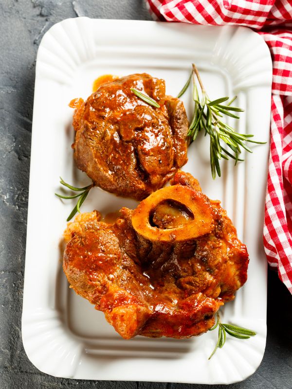 Spanish osso buco on a white plate decorated with thyme. Perfect Spanish Beef Osso Buco Recipe