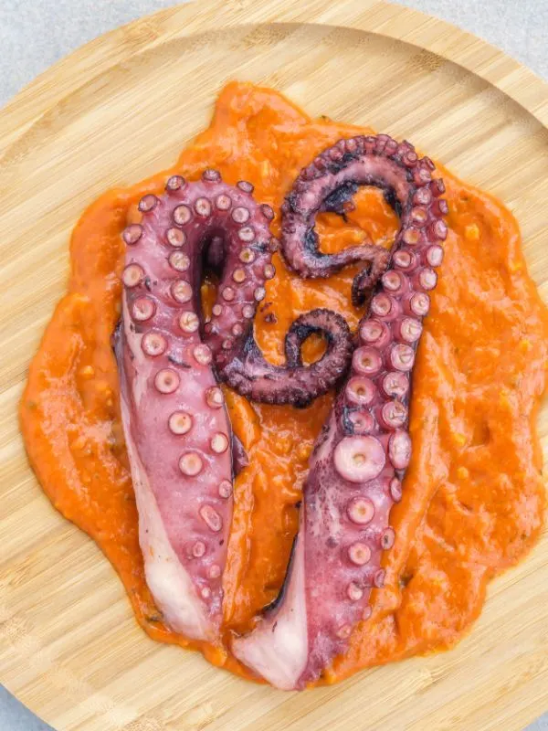 Spanish romesco sauce with octopus on a wooden plate.