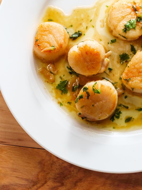 Spanish scallops on a white plate with garlic and butter sauce.