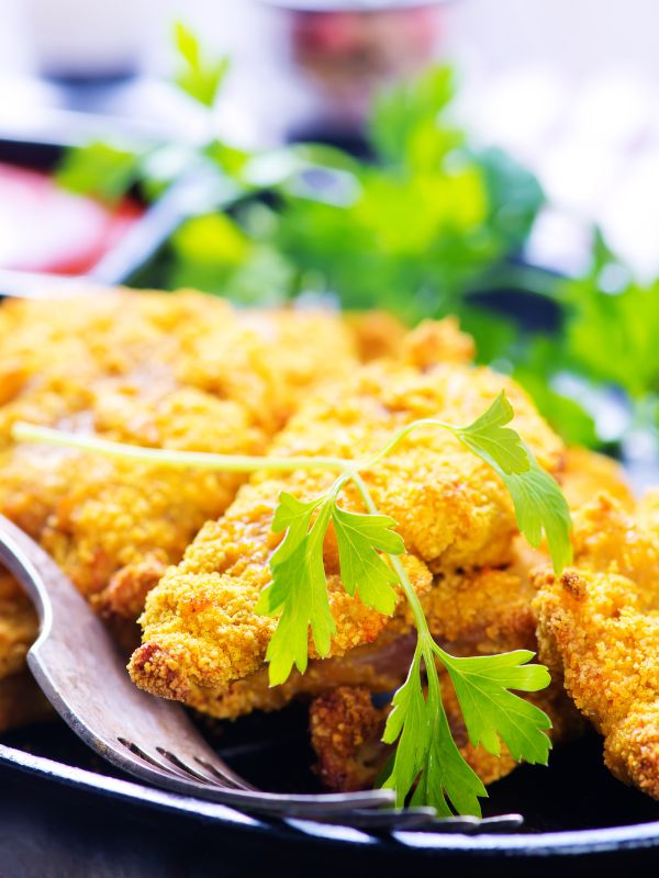 closeup with Spanish fried fish served with sauce and decorated with fresh parsley.