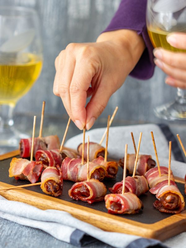 dates wrapped in bacon a serving plate and a women with a glass of wine in her hand