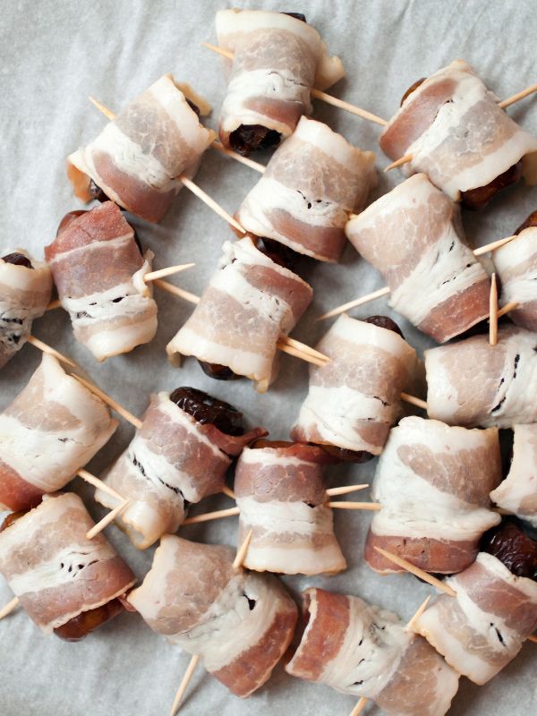 dates wrapped in bacon on a kitchen towel ready to be fried