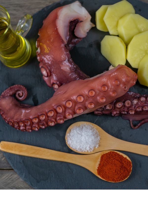 ingredients for spanish octopus recipe such as octopus, potatoes, salt and paprika on a black plate.