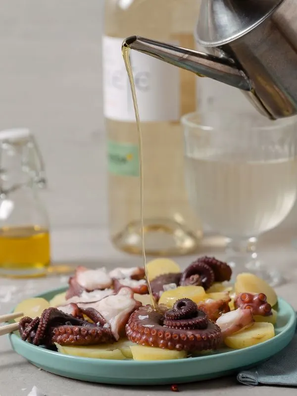 olive oil being pored over spanish octopus recipe with a bottle of wine in the background.