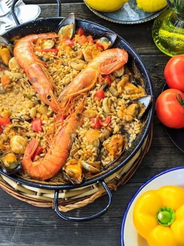 paella in a pan with vegetables next to it that  were used to make the spanish sofrito recipe.