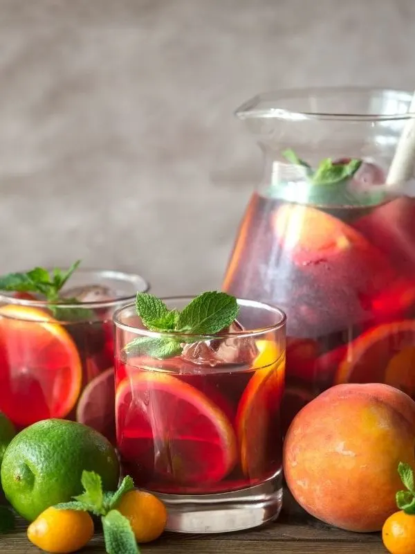 sangria in a jar surrounded by fruits like oranges, limes and peaches.