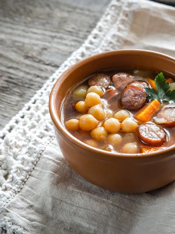 garbanzo bean soup with chorizo in a clay bowl on a wooden table.