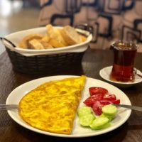 spanish omlet recipe on a plate with fresh tomatoes and cucumber and bread and tea in the background.