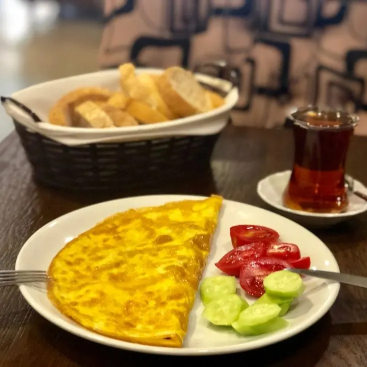 spanish omlet recipe on a plate with fresh tomatoes and cucumber and bread and tea in the background. - Easy Spanish Omelet Recipe
