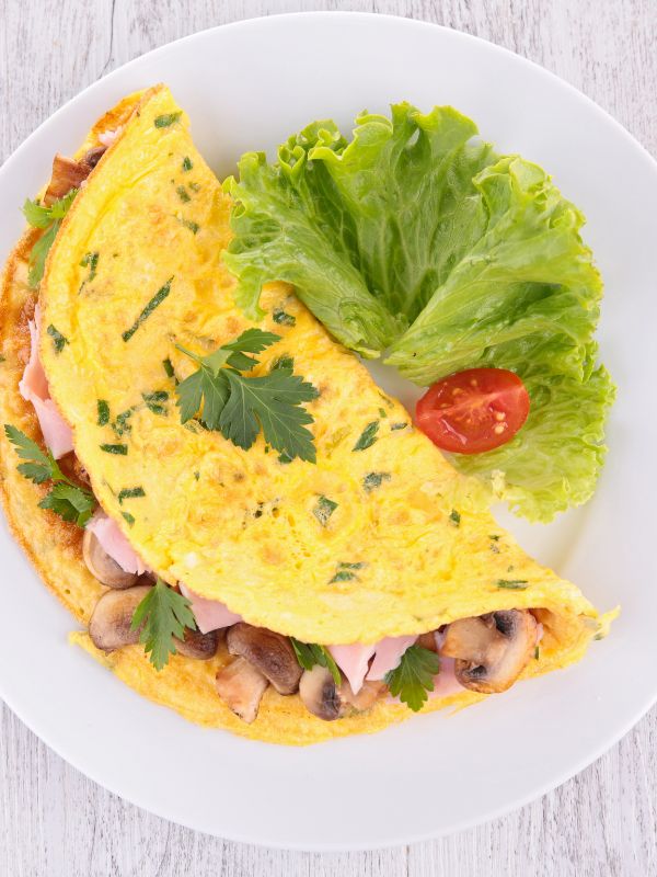 spanish omelet with mushrooms and ham on a white plate with a salad leaf next to it.