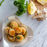 spanish scallops in a bowl with lemon, garlic and parsley next to it.
