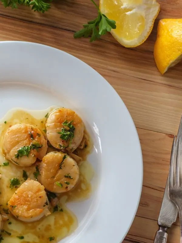 spanish scallops in a white plate with fresh lemon next to it. 25 Best Spanish Seafood Recipes to Try at Once!