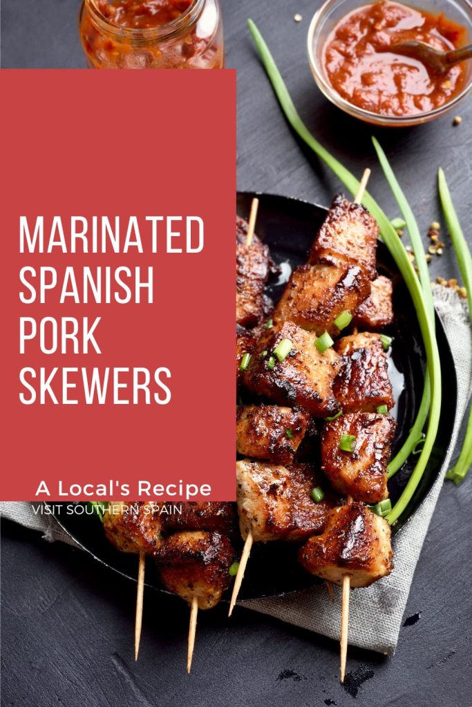 Spanish pork skewers on a black plate. On the left it's written Marinated Spanish pork skewers.