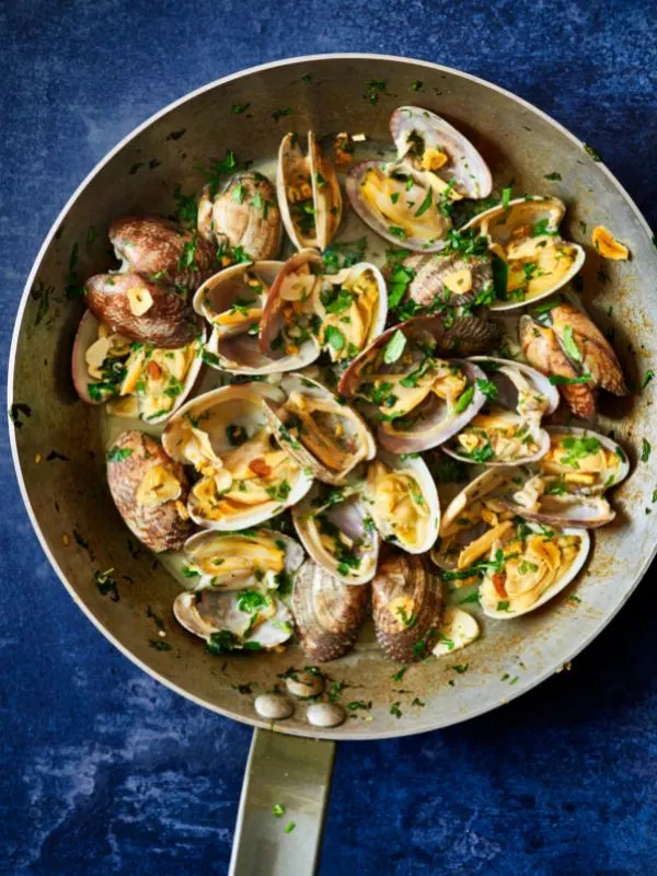 Spanish clams with chorizo in a pot on a blue surface.