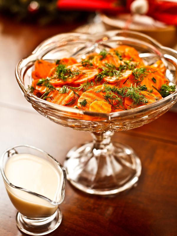Spanish marinated carrots in a glass bowl with a sauce next to it.
