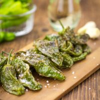 Spanish padron peppers on a wooden board with a drink in the background
