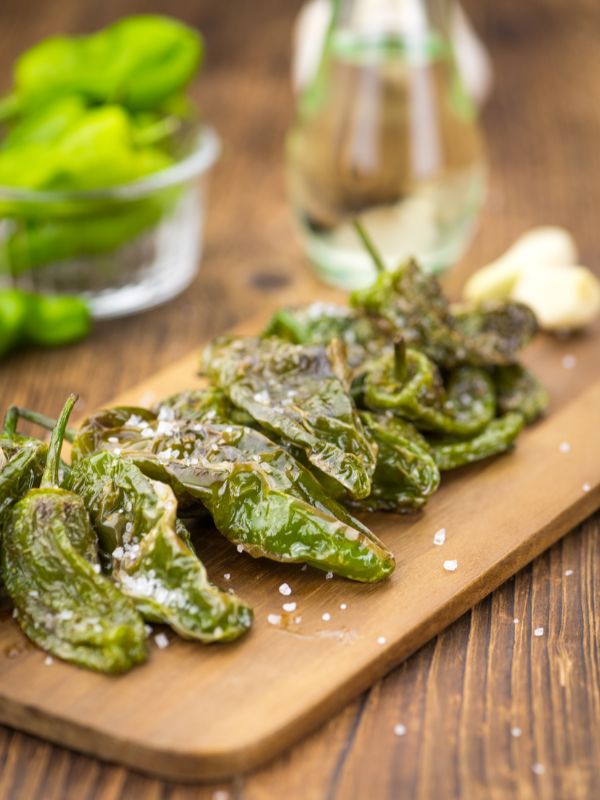 Spanish padron peppers on a wooden board with a drink in the background - Best Spanish Padron Peppers Recipe