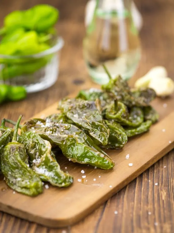 Spanish padron peppers on a wooden board with a drink in the background