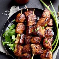 Spanish pork skewers on a black plate with red sauce next to them, Best Pork Recipes from Spain