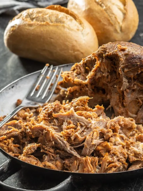Spanish pulled pork recipe in a pot with 2 buns of bread next to it
