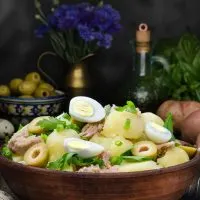 Spanish tuna salad in a wooden bowl with potatoes, olives and olive oil in the background
